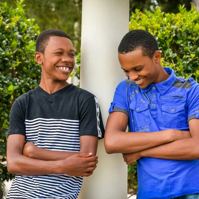 Two teenagers leaning on a post outdoors, laughing together